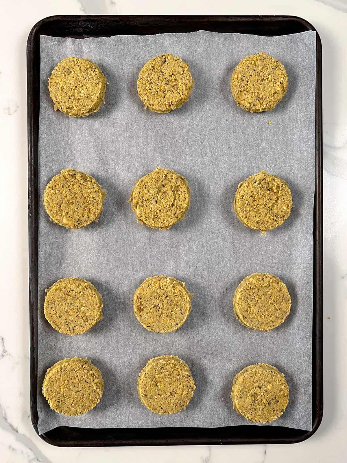 a black tray lined with paper with 12 uncooked frozen falafel balls