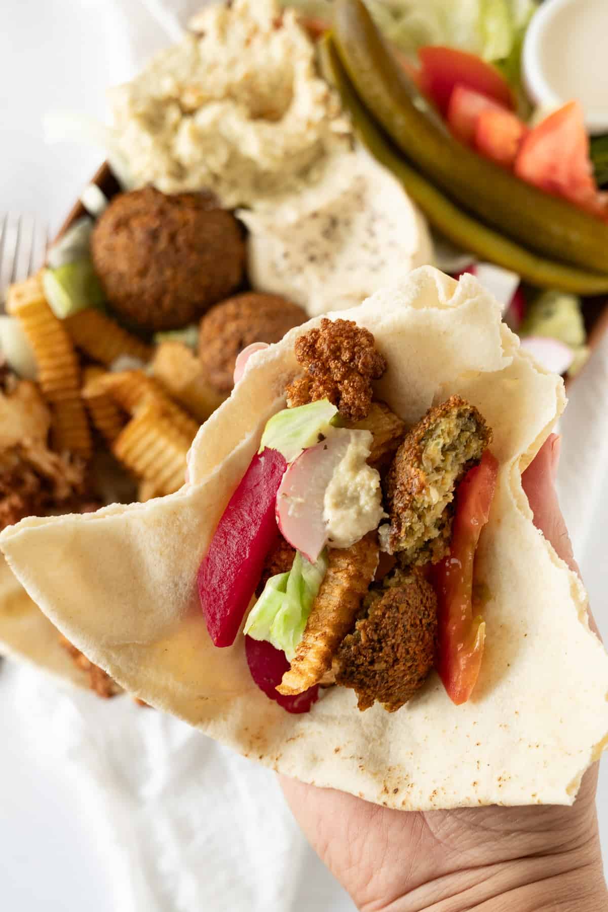 a hand holding a piece of pita bread with falafel and veggies and sauce