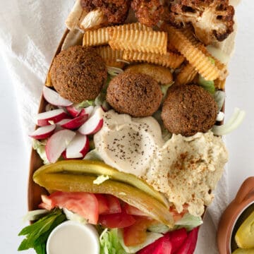 a long bowl of falafel, salads, pink and green pickles, whiteish dips and fries and fried cauliflower
