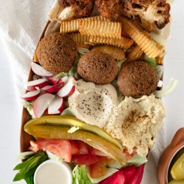 a plate of falafel, veggies, fries, dips and sauces