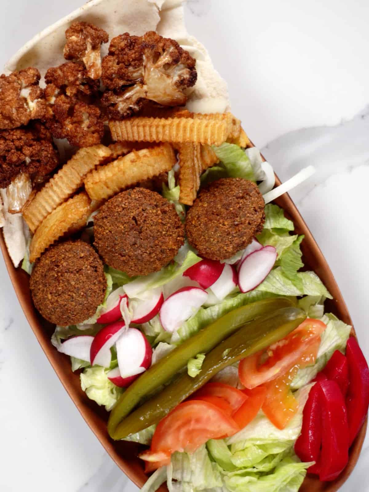 falafel, chopped vegetables, fries, fried cauliflower florets, pink pickles and pita bread in a bowl