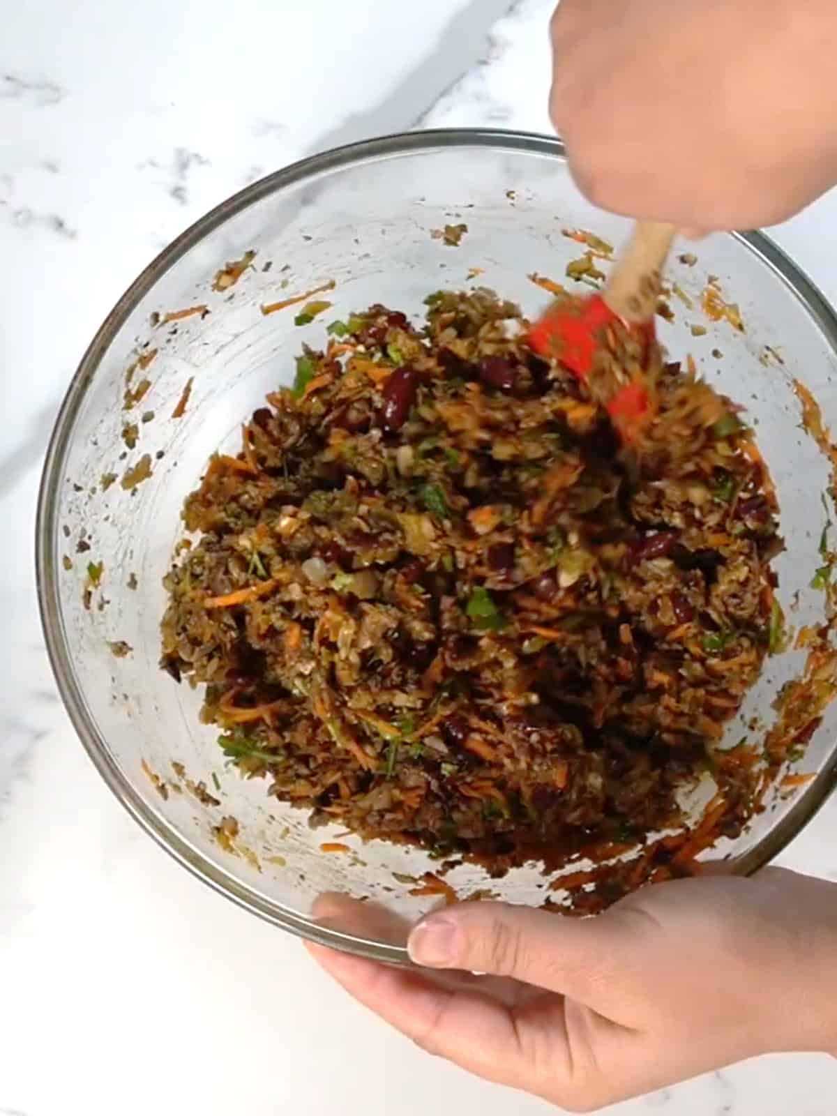 finely chopped vegetables in a glass bowl being mixed by female hands