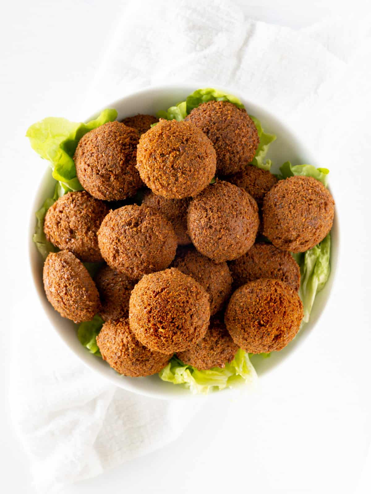 a white round plate filled with brown falafel bowls with green lettuce underneath