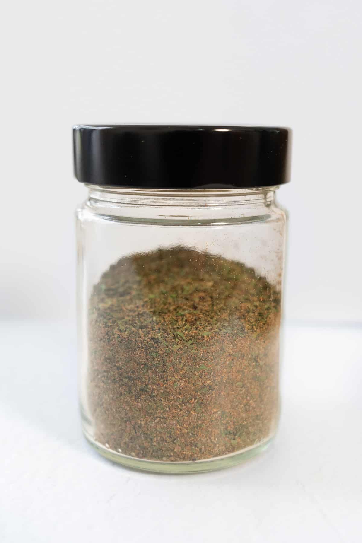 a glass jar with a black lid filled with falafel spice blend