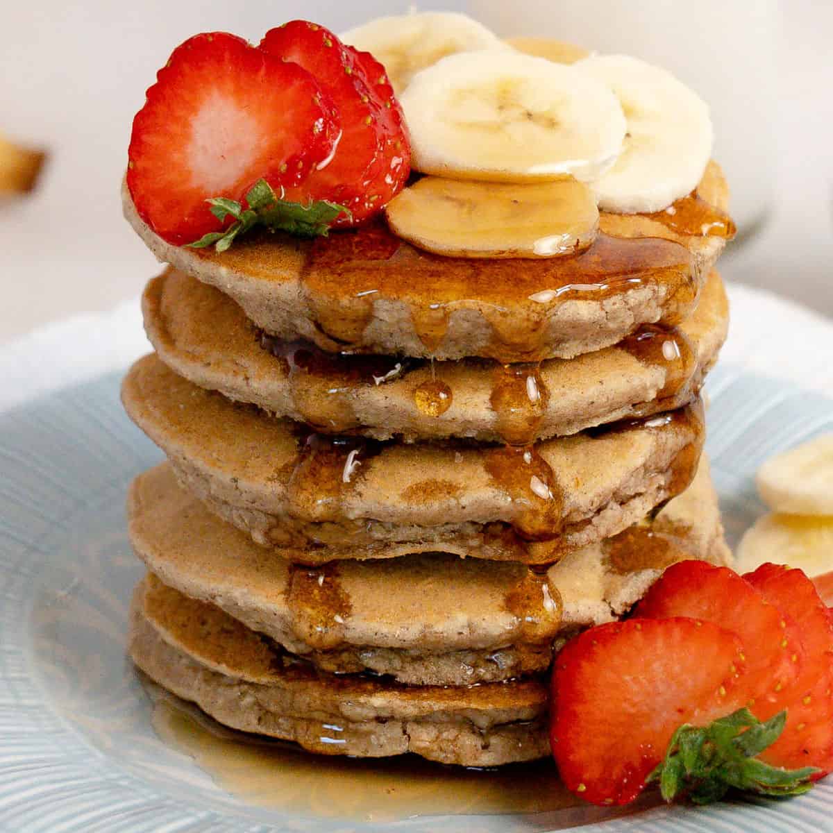 a tall stack of pancakes with syrup and fruit