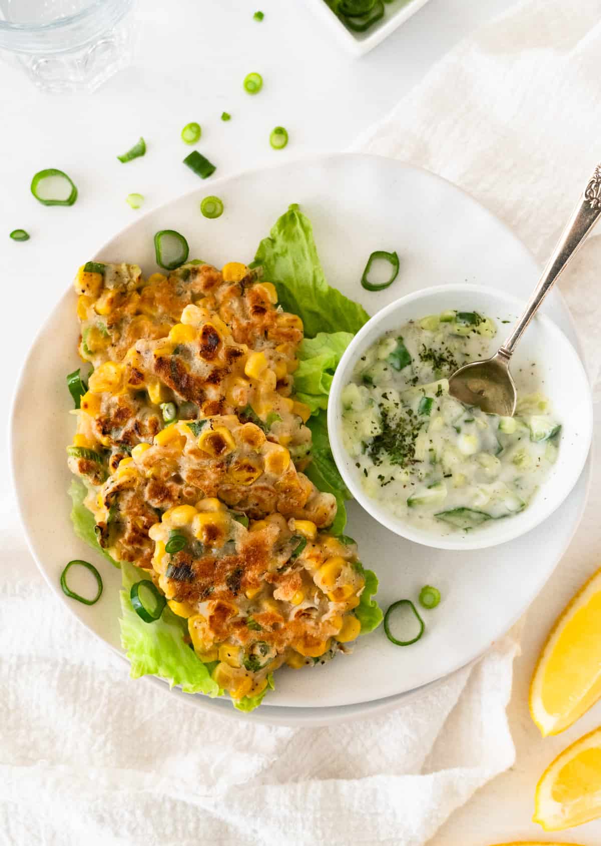 four vegan corn fritters on a white plate with cucumber yogurt dip on the side