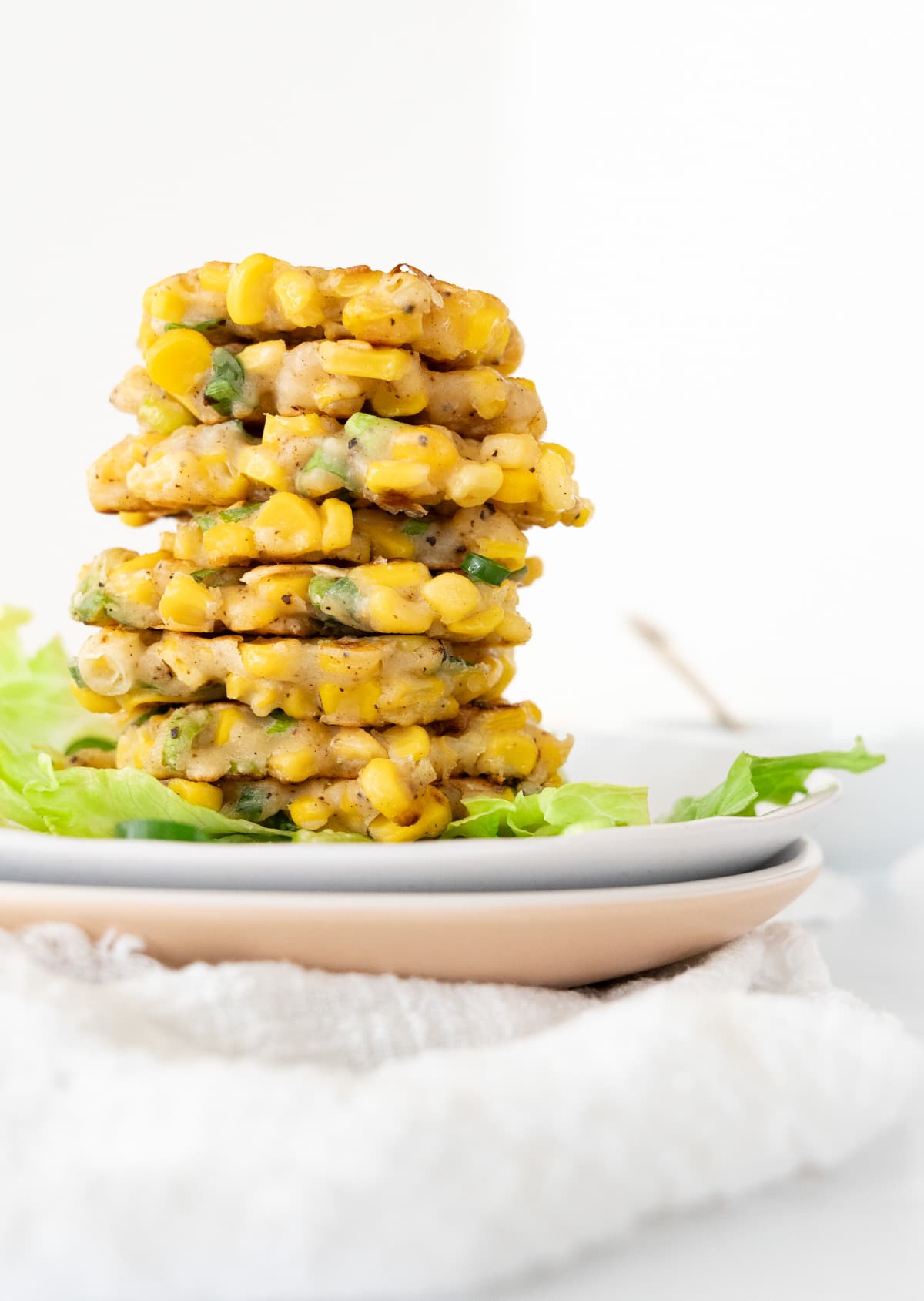 a stack of small corn fritters on two plates with green lettuce