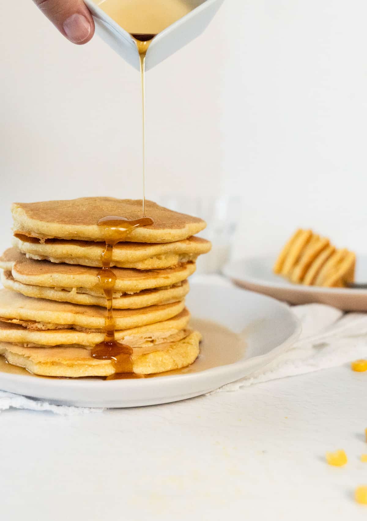 a stack of corn pancakes with maple syrup being poured on top