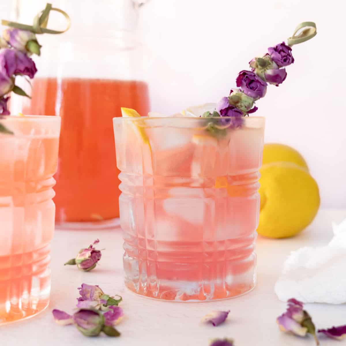 a glass of pink rose lemonade garnished with a stick of dried roses