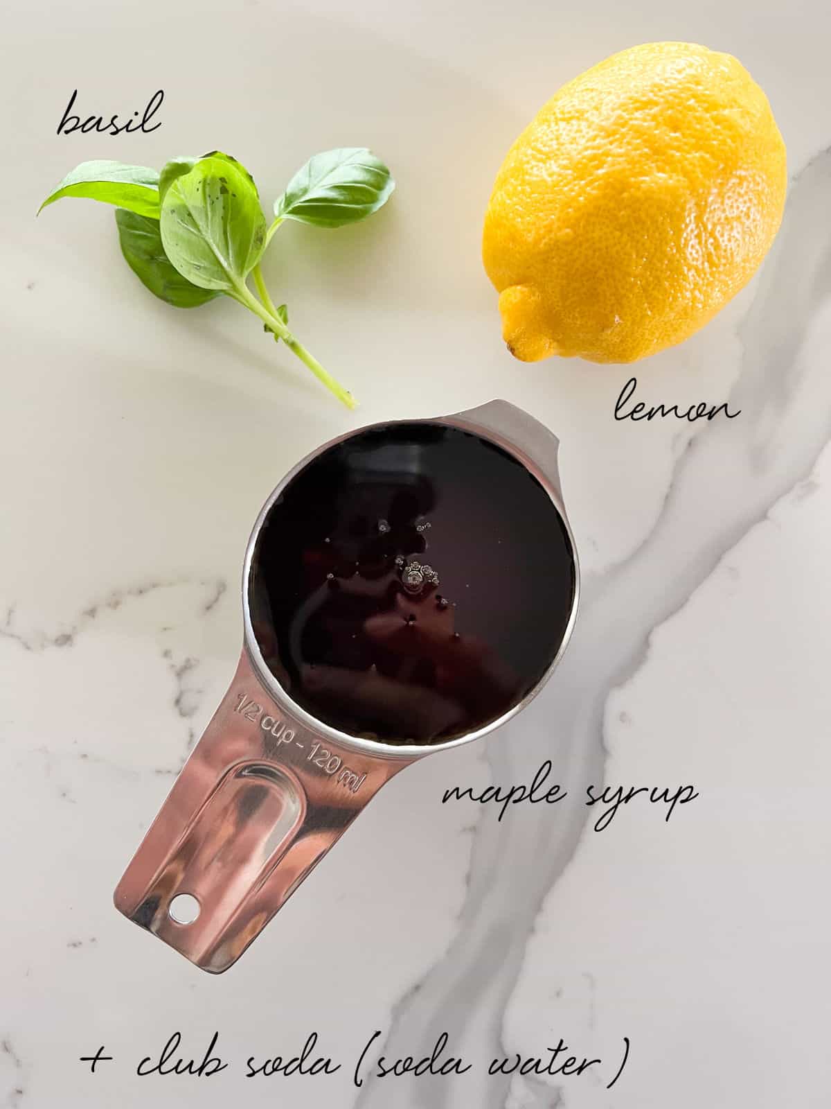 a lemon, basil leaves and a measuring cup of maple syrup