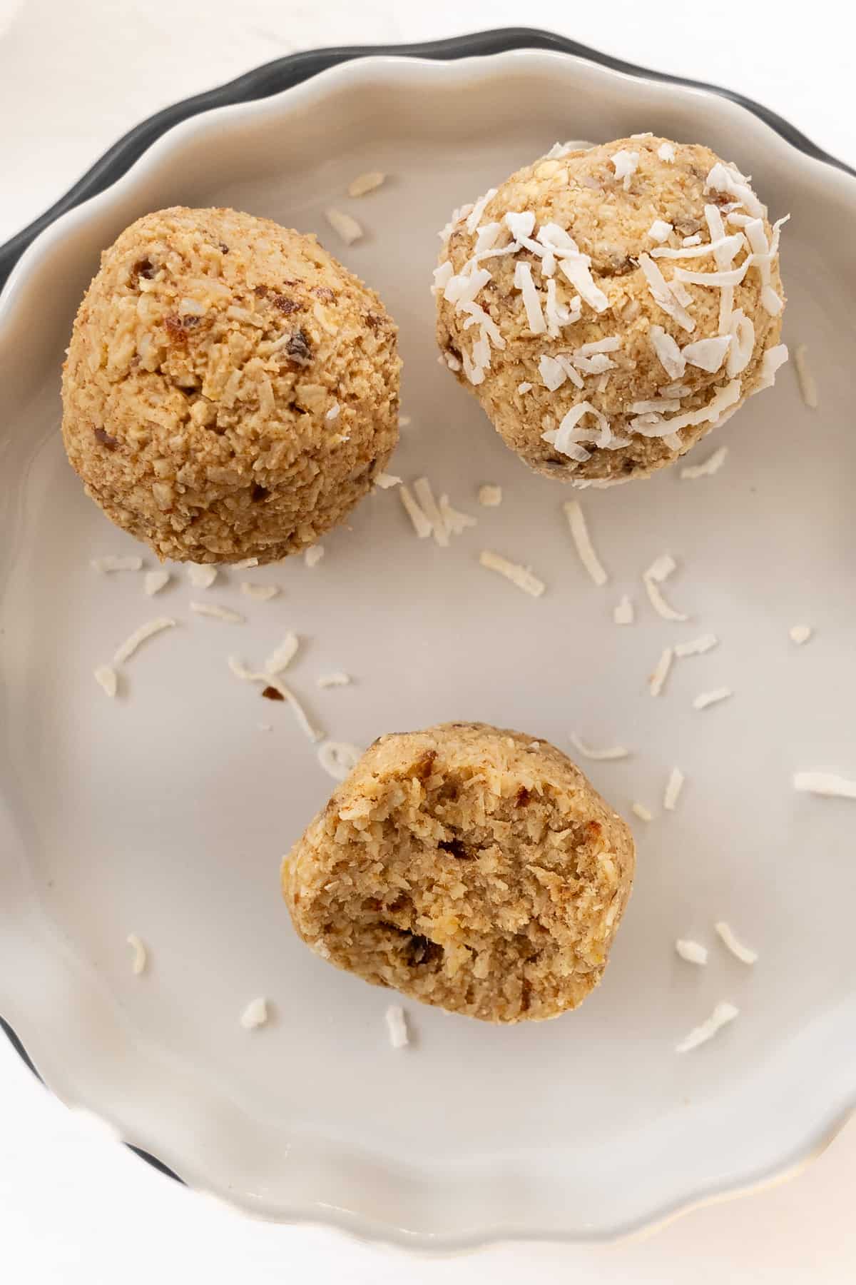 three coconut lemon balls in a bowl one with a bite missing