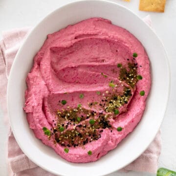 a white bowl with pink beetroot hummus in it