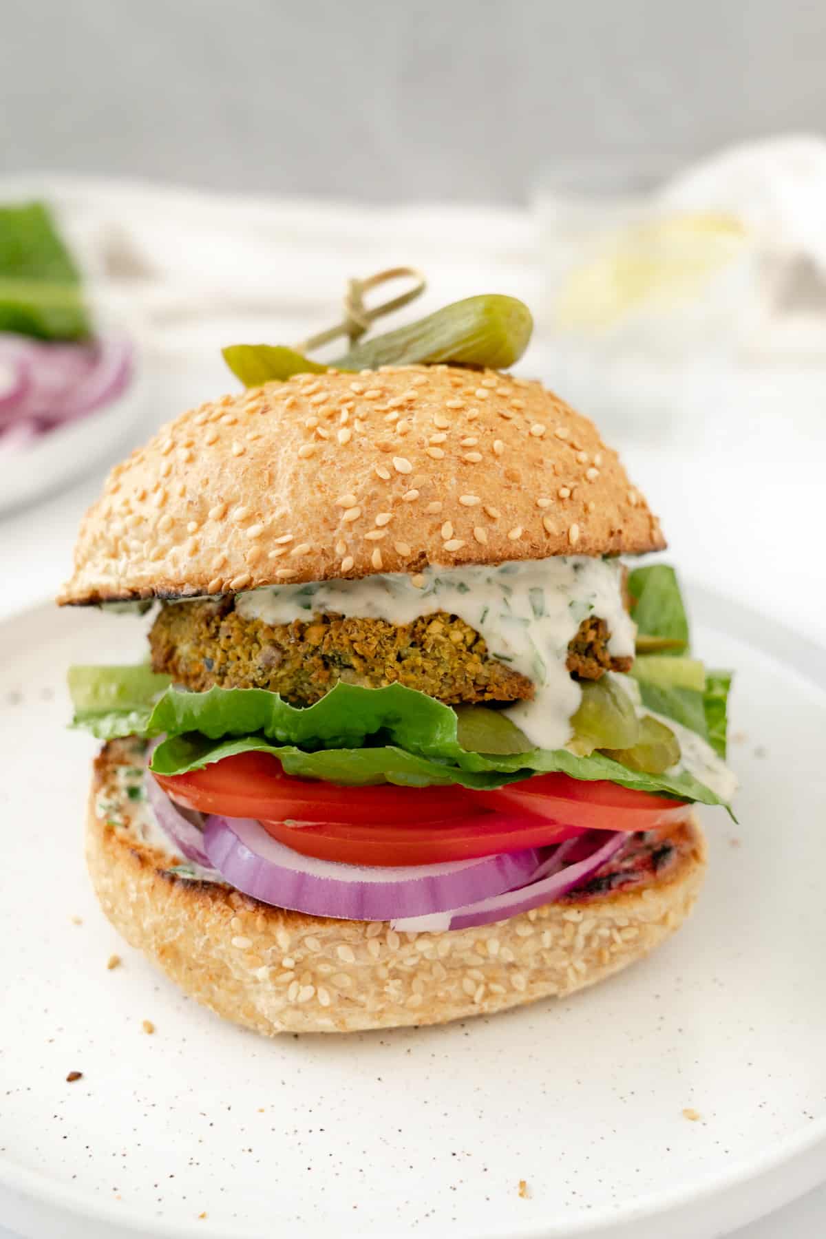 a falafel burger sitting on a white plate with tahini sauce dripping from it