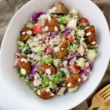 a white bowl with falafel salad in it and gold cutlery on the side