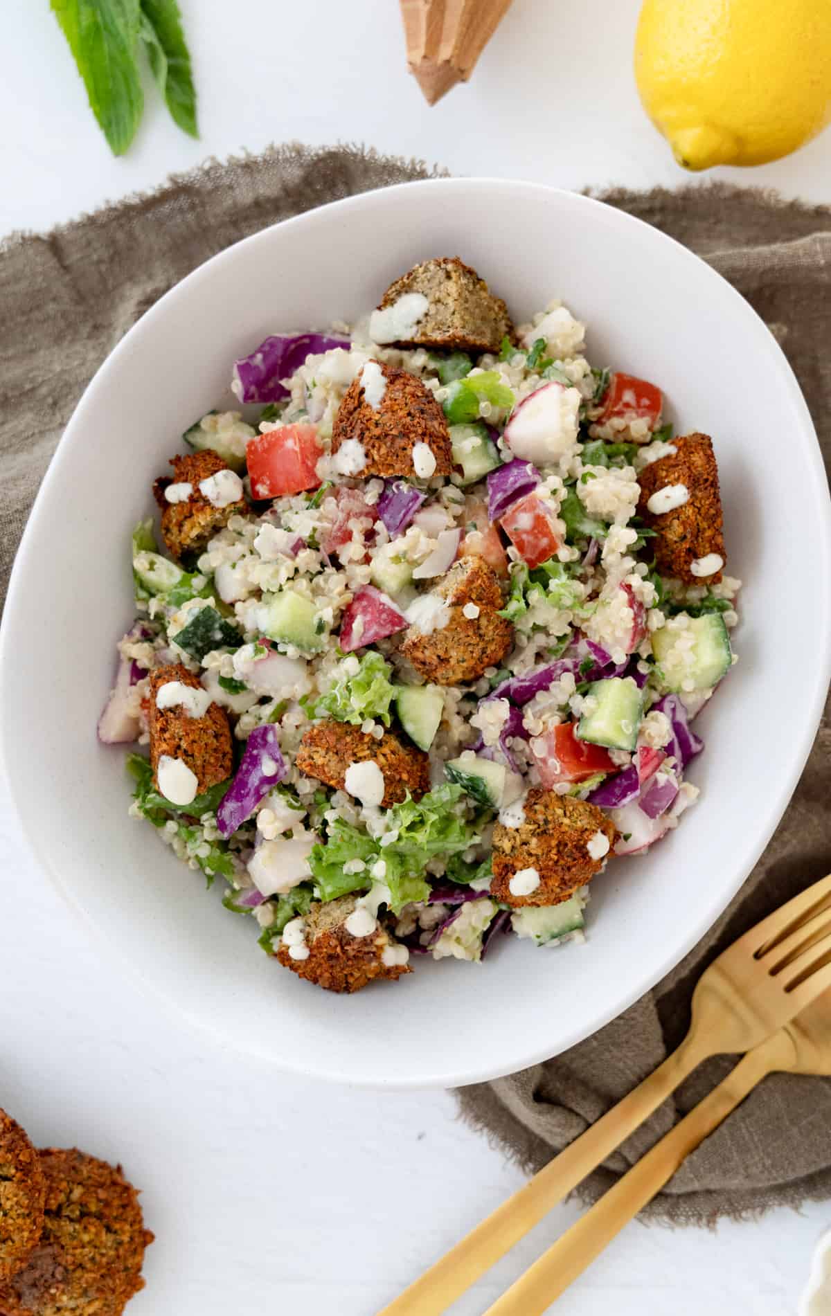 a white bowl with falafel salad in it and gold cutlery on the side