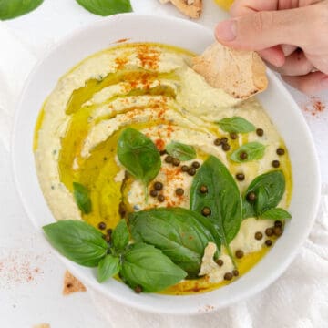 a male hand dipping in a pita chip into basil hummus