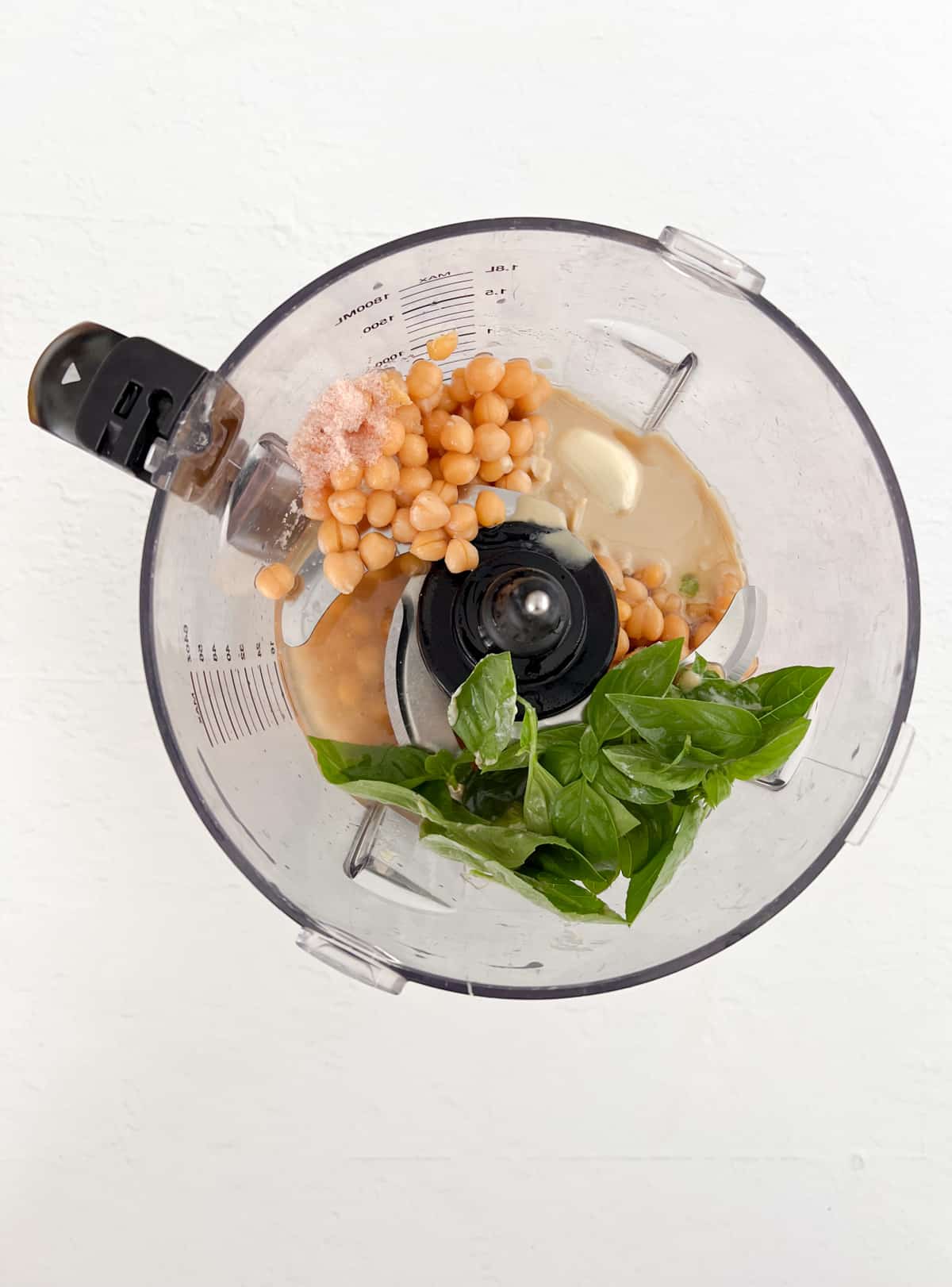 unprocessed basil hummus ingredients in a food processor bowl