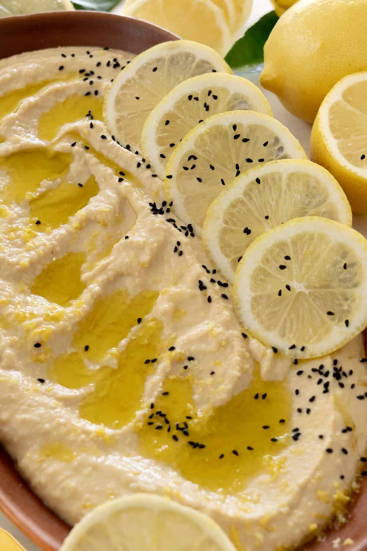 a plate of lemon hummus wth black seeds on top surrounded by lemons