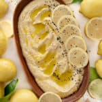 a plate of lemon hummus wth black seeds surrounded by lemons