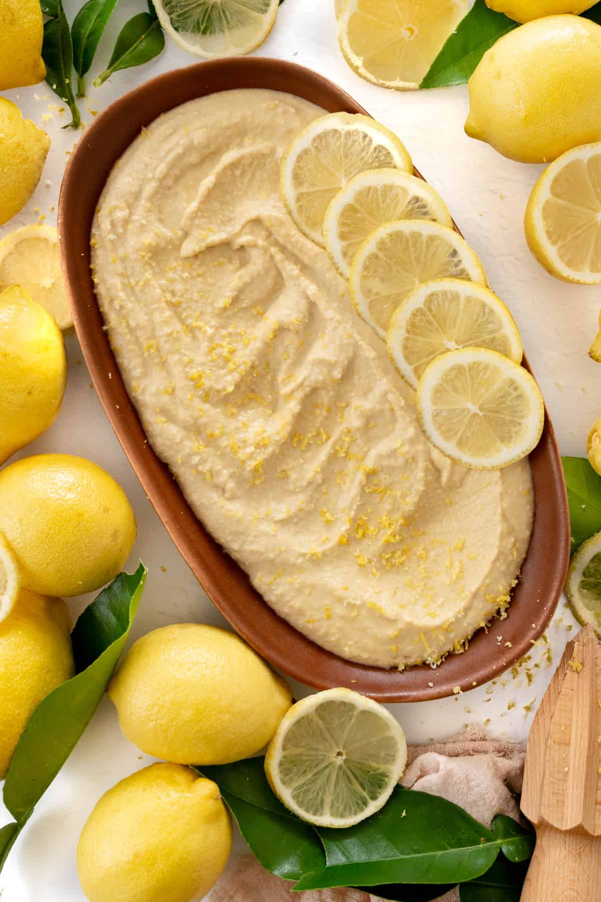 lemon hummus covered in lemon zest in a plate with lemons on the side
