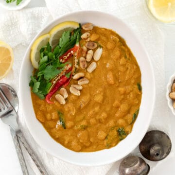 a bowlful of peanut butter curry garnished with herbs, peanuts and chili