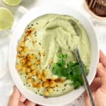 two hands holding a bowl of cilantro lime hummus
