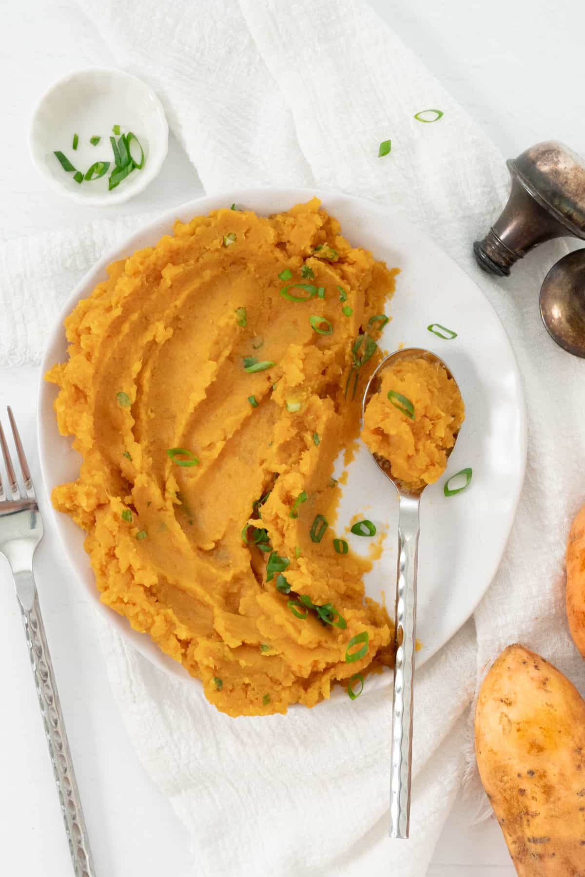 a white plate and a silver spoon with vegan mashed sweet potato in them