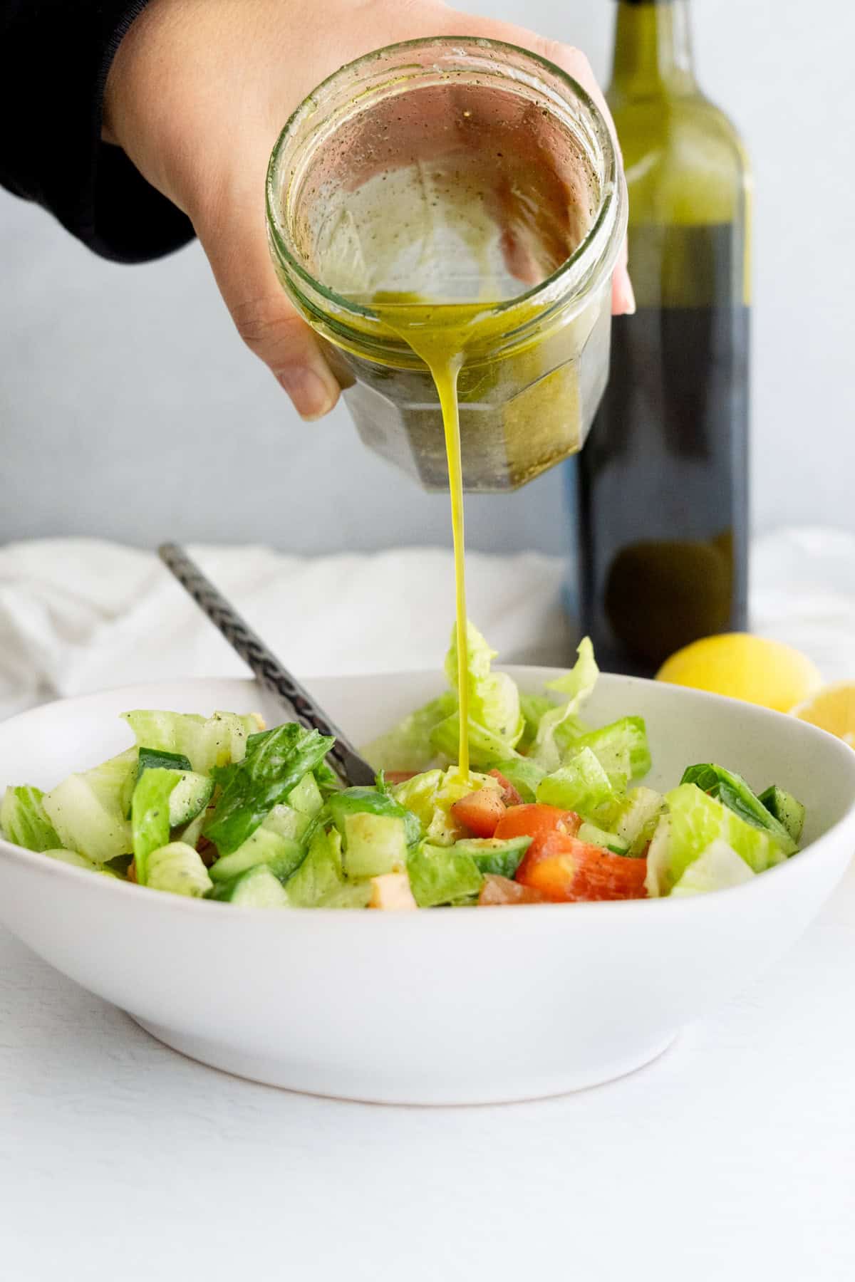 a hand pouring Lebanese salad dressing out of a glass jar onto salad
