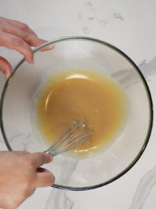 hands whisking tahini, maple syrup and salt in a glass bowl