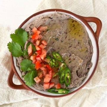 a bowl of vegan black bean dip topped with tomatoes, chili and cilantro