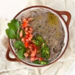 a bowl of vegan black bean dip topped with tomatoes, chili and cilantro