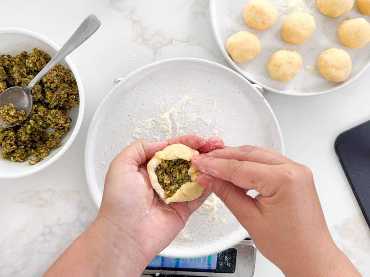 hands closing maamoul dough with filling in it