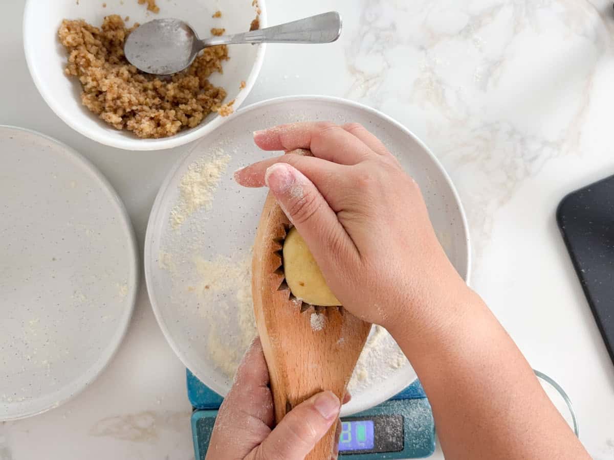 hands pressing a filled dough ball into a maamoul press