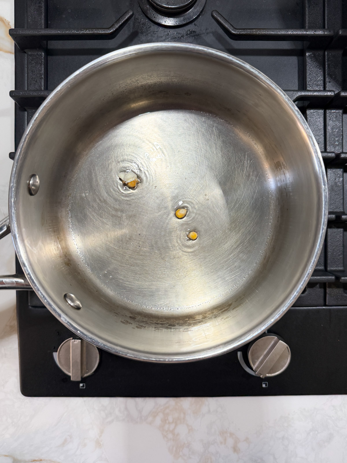 three corn kernels in oil in a pot