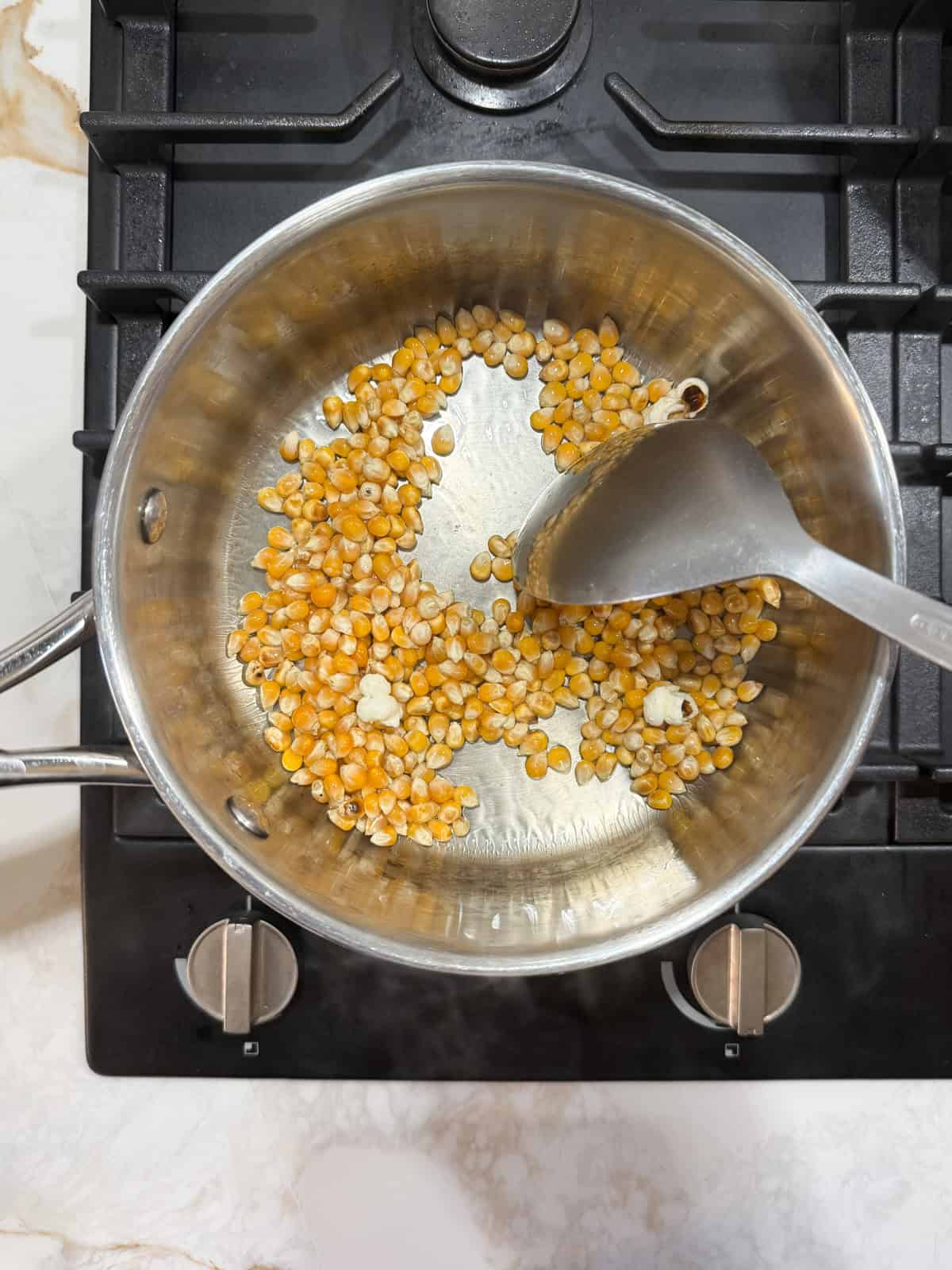 corn kernels in oil in a pot with a spoon