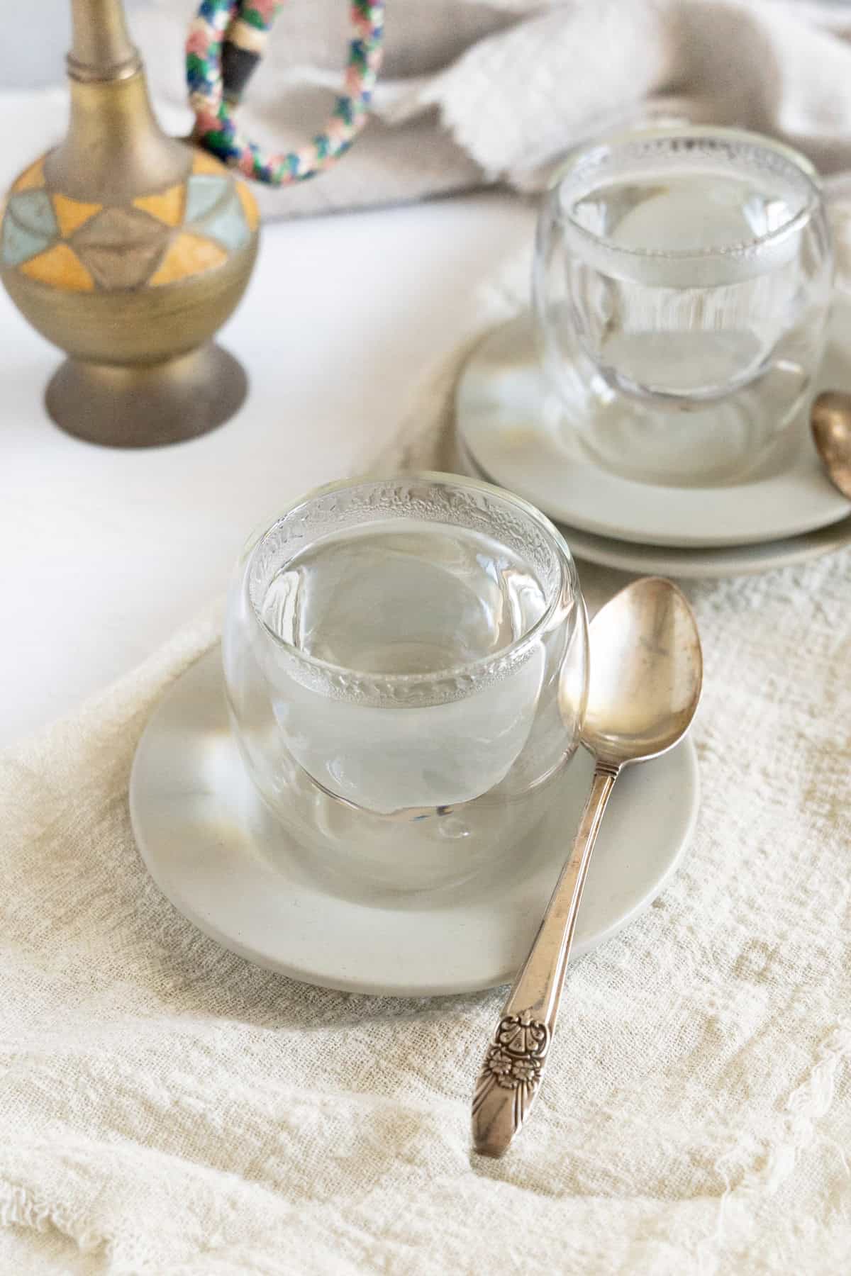 Two clear glass cups on white saucers with gold spoons filled with Lebanese white coffee