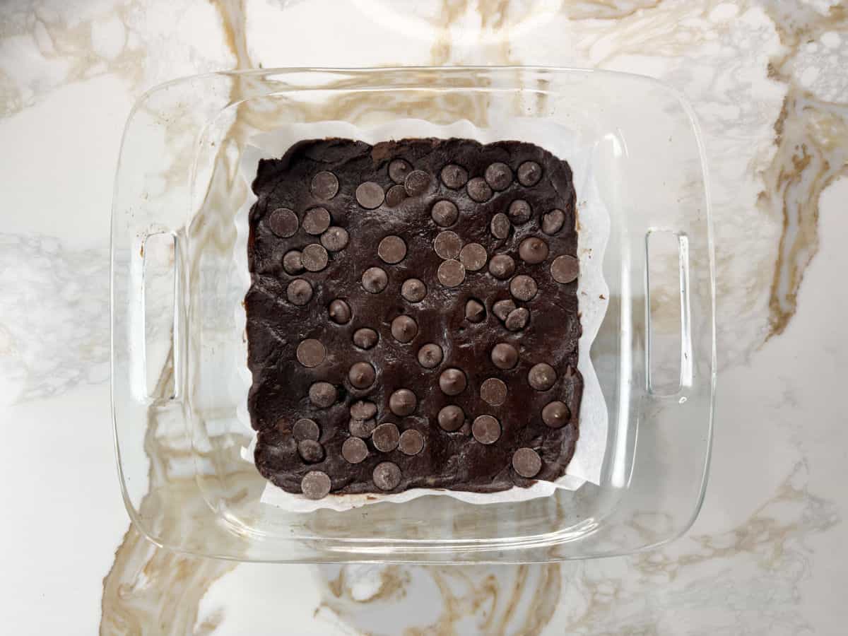 chickpea brownie batter spread out in a baking tray with choc chips on top