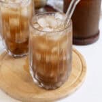 Refreshing plant-based iced coffee with ice cubes in a glass, served on a wooden tray.