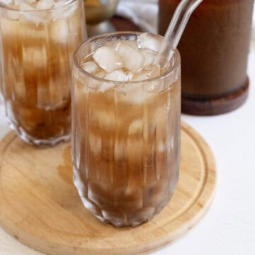 Refreshing tamarind juice with ice cubes in a glass, served on a wooden tray.