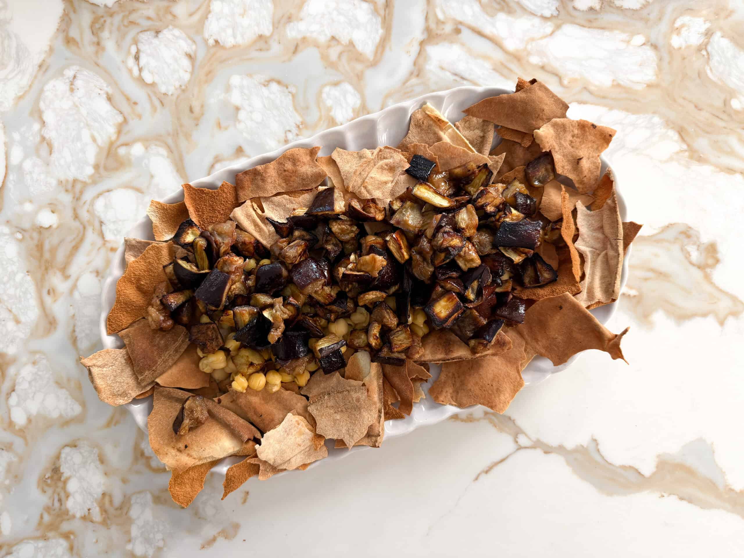 crispy broken pita bread with chickpeas and roasted eggplant pieces on a white plate