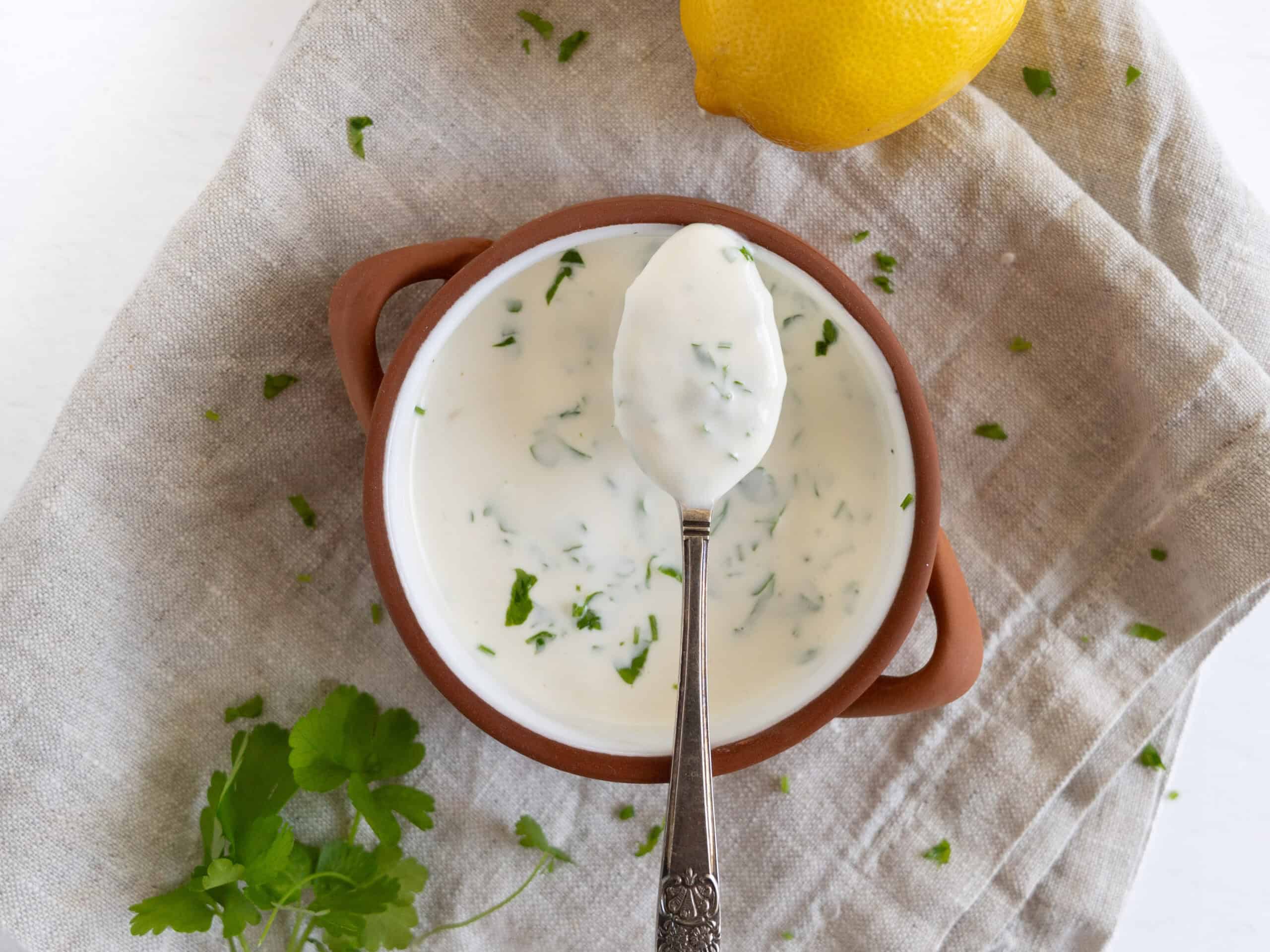 a bowl of yogurt tahini sauce with parsley flecks through it