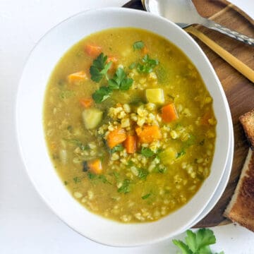 Healthy veggie barley soup with carrots, zucchini, and fresh cilantro in a white bowl.