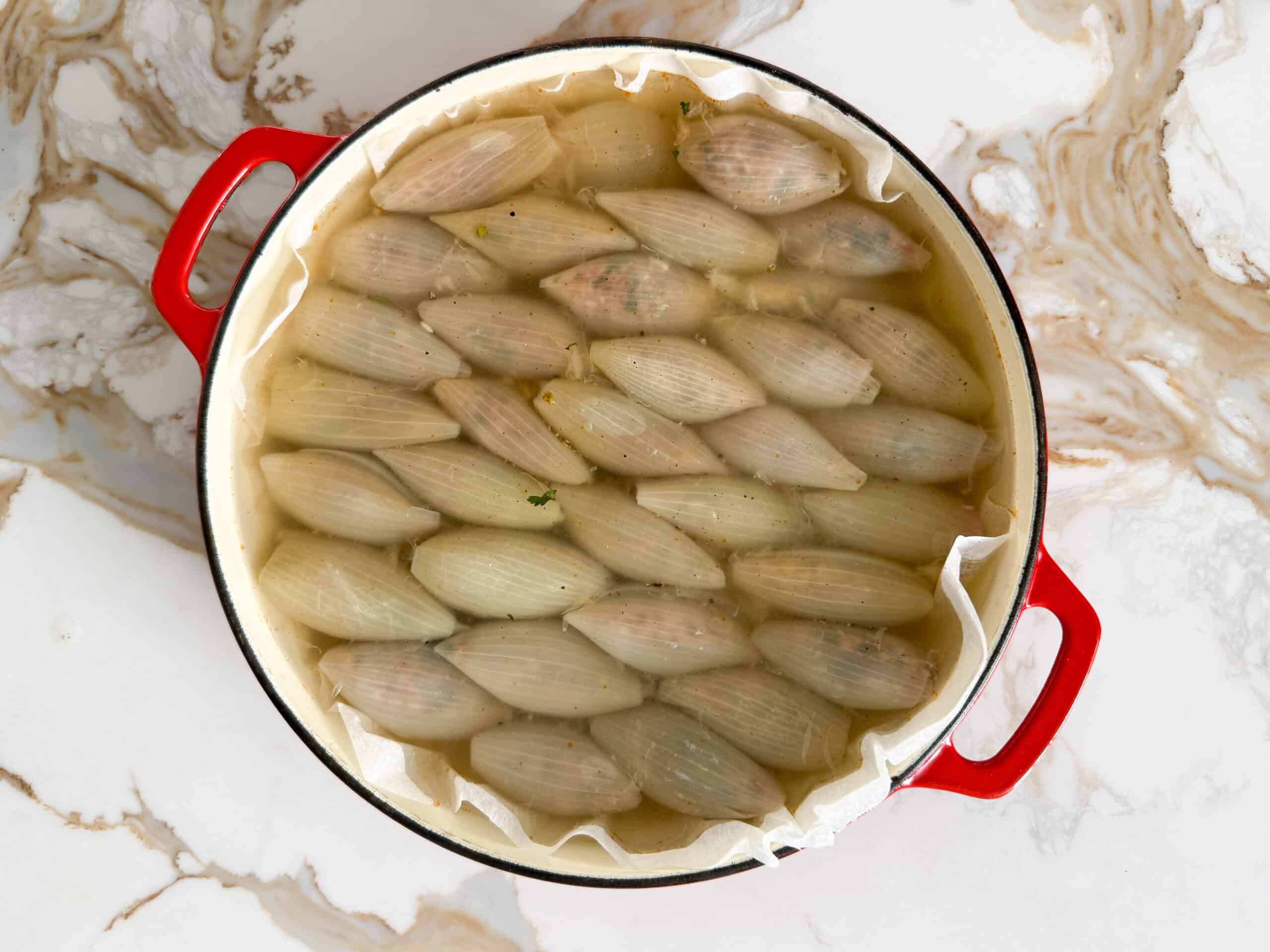 stuffed onion rolls in a casserole dish submerged in water