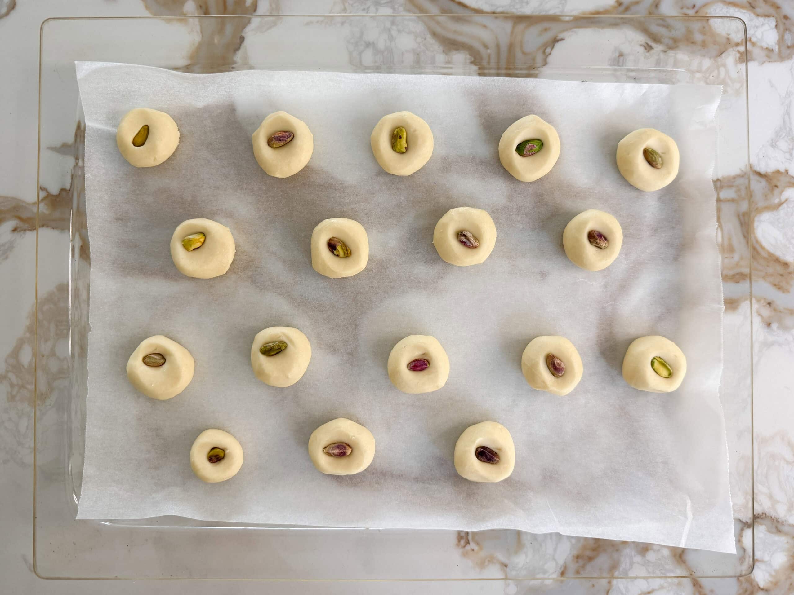 unbaked ghraybeh cookies with pistachio on top in a baking pan